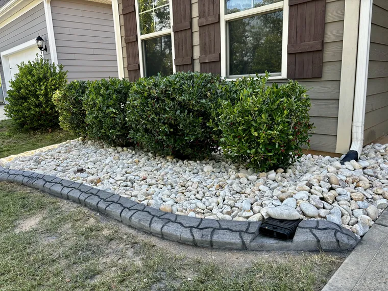 Stamped concrete curb with river rock and a built-in rain drain