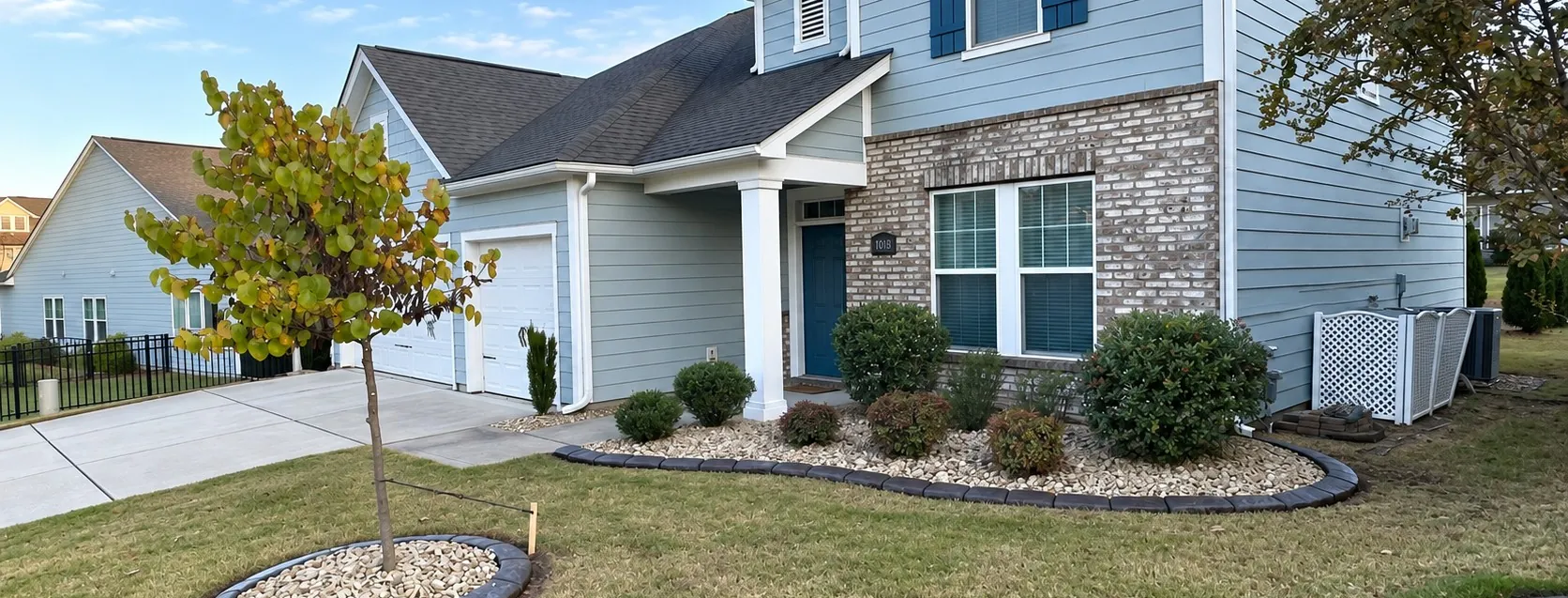 A finished front yard with a river-rock bed, a tree ring and a poured curb