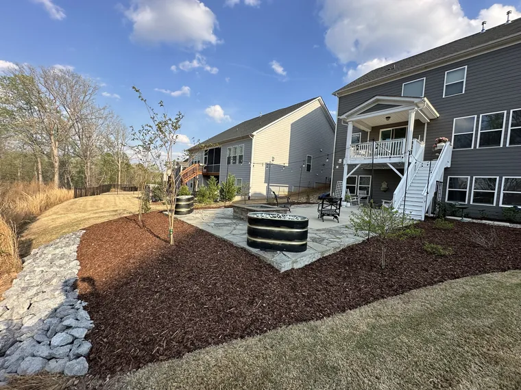 A backyard with mulched beds, a patio and a rock drainage runnel