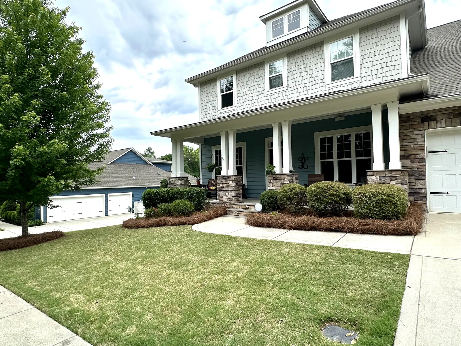 Two-story house with a green lawn and foundation shrubs along the porch