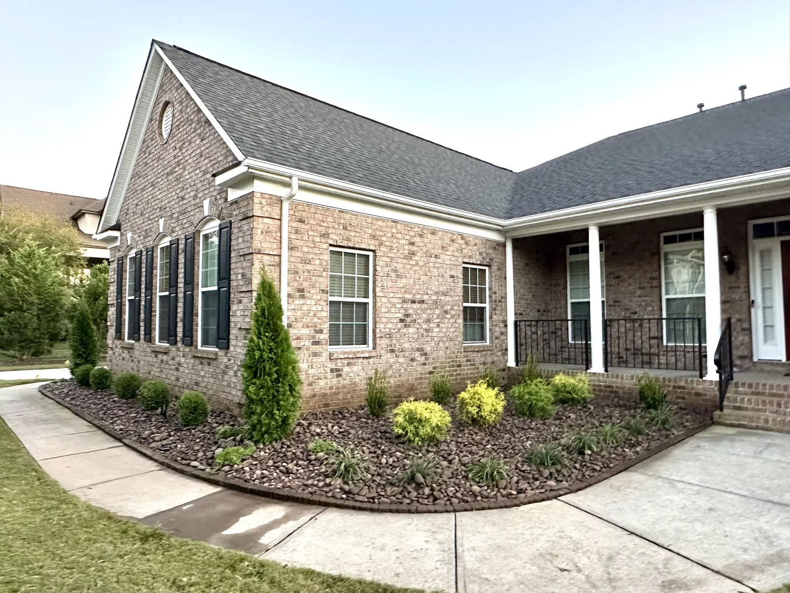 Brick ranch with a foundation bed of river rock, evergreens and small shrubs