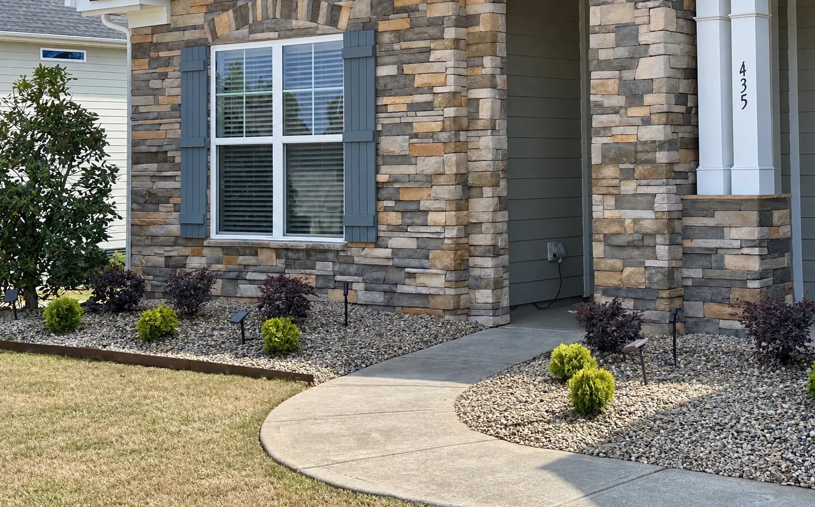Stacked-stone facade with a low gravel bed, small shrubs and path lighting