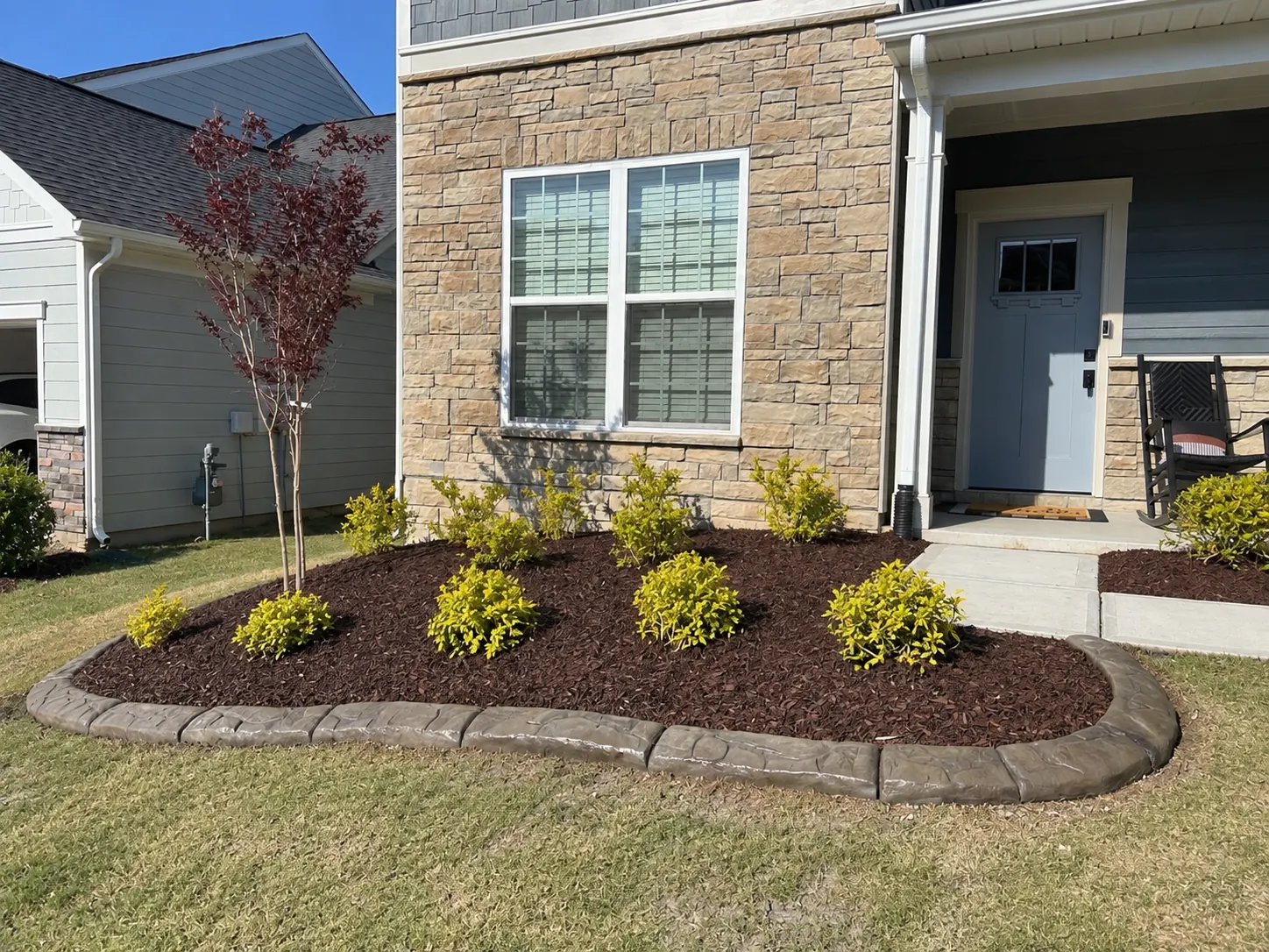 Stone-faced house with a mulched oval bed, gold shrubs and a poured curb