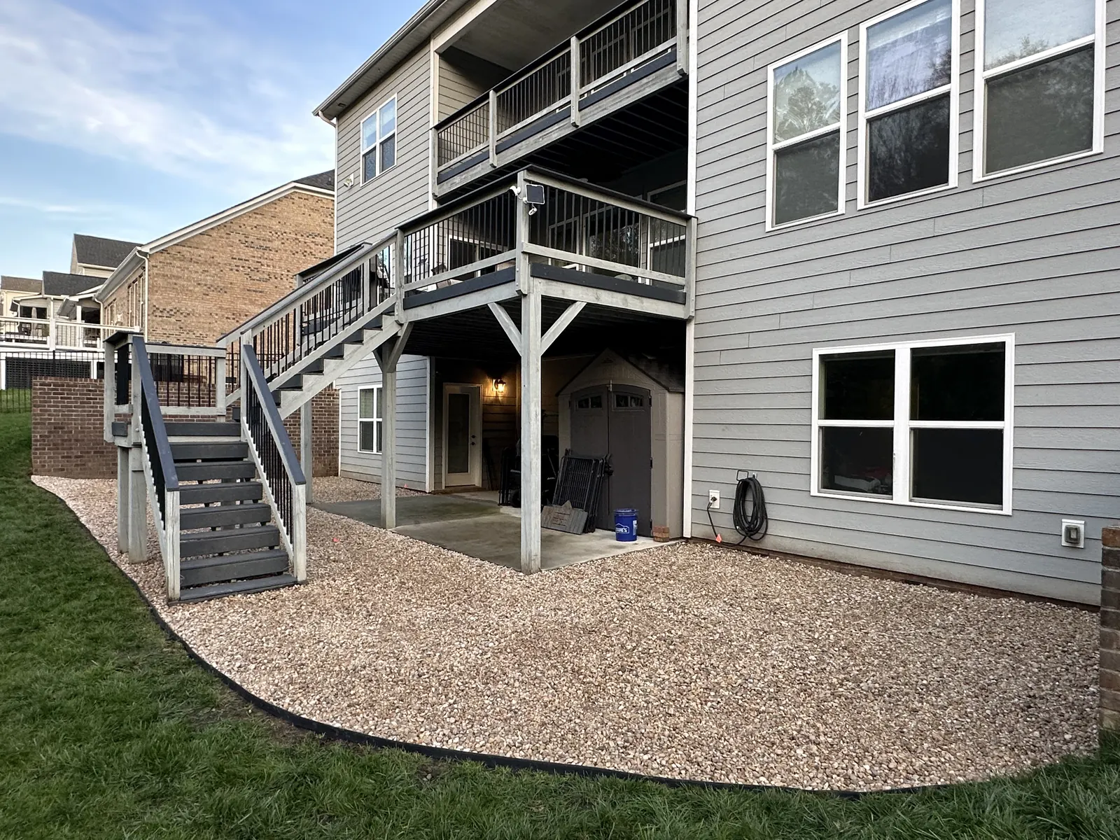 Pea gravel under a rear deck, edged with a dark curb against the lawn